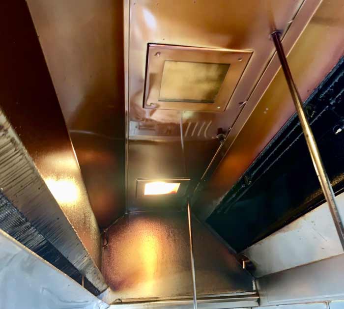 Commercial kitchen hood canopy coated in a yellow grease film indicating the need for professional sanitation and maintenance.