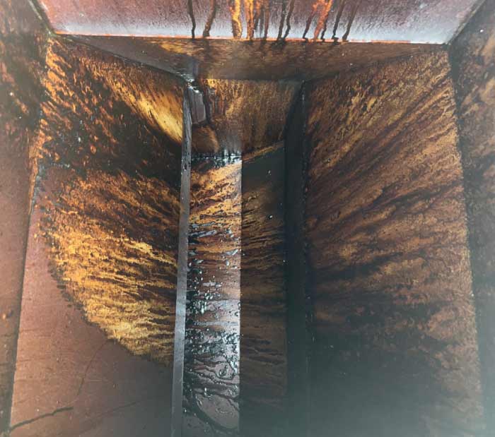 Vertical commercial kitchen exhaust duct coated in heavy grease buildup presenting a critical fire hazard before cleaning.