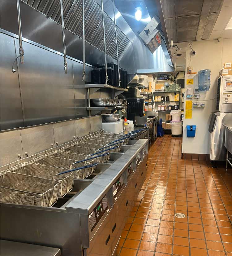Full view of a commercial kitchen fryer line and exhaust hood system in a San Diego food establishment.
