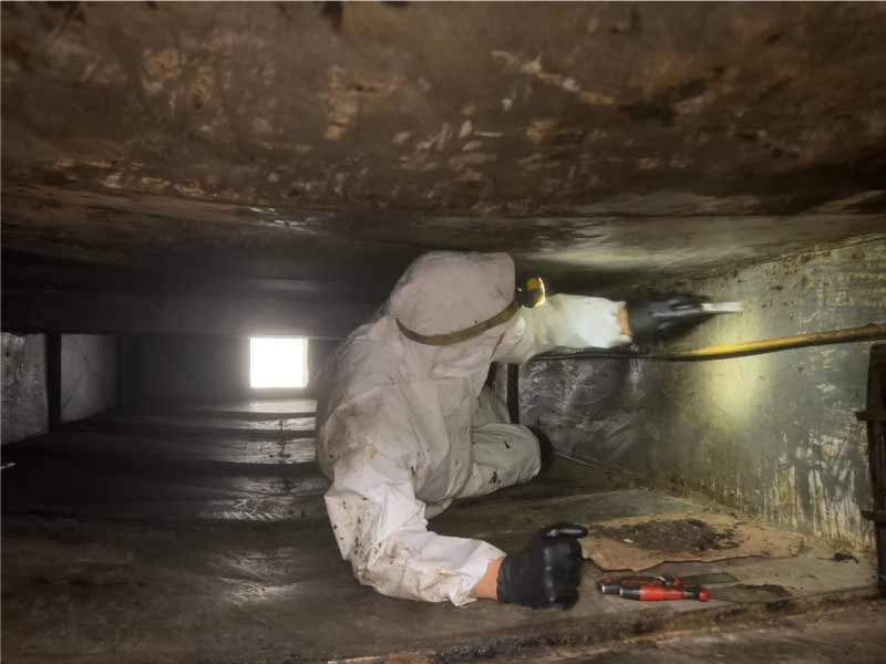 Certified technician in protective gear manually scraping grease from inside narrow exhaust ductwork to remove hidden fire risks.