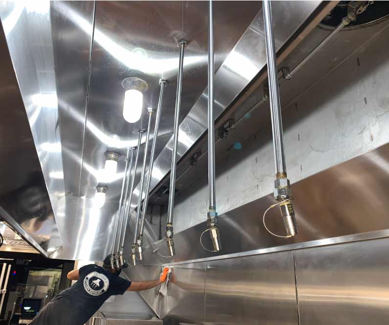 California Kitchen Exhaust technician wiping down stainless steel surfaces during a deep cleaning kitchen exhaust hood service.