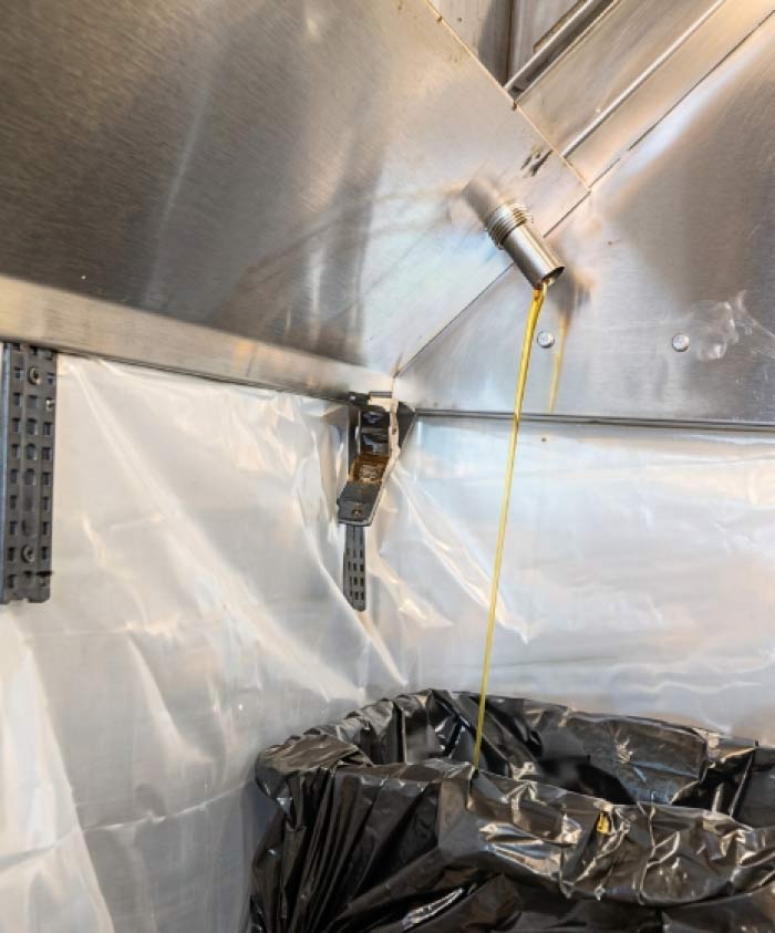 Grease draining from a commercial hood drain into a lined bag during kitchen hood cleaning in Downtown San Diego