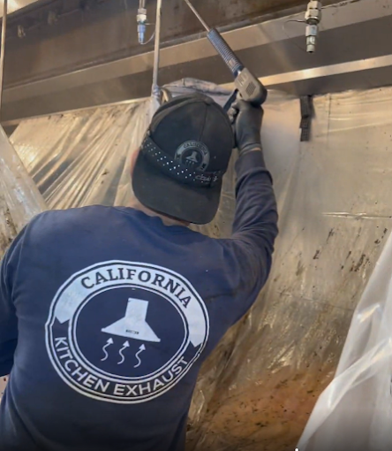 California Kitchen Exhaust technician pressure washing the inside of a commercial kitchen hood protected with plastic sheeting